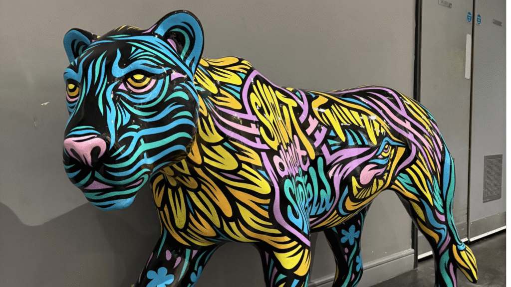 An image of a majestic painted lioness against a plain grey background. Her colours are vibrant and an all-over design sees her covered in blues, greens, pinks, purples, oranges and yellows!