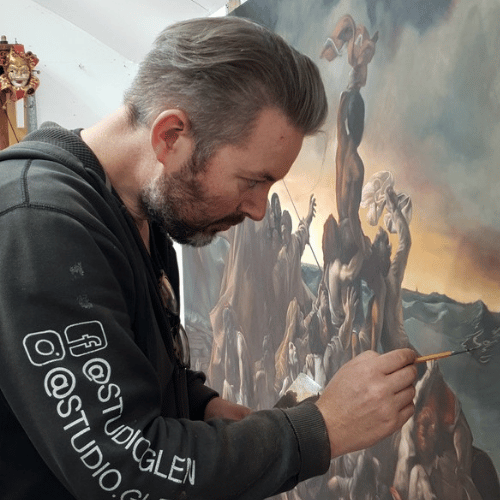 A person with short hair and a beard, wearing a black hoodie is side-on working on an intricate artwork.