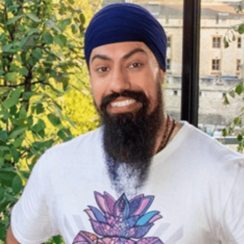 A man with a beard wearing a white t-shirt looks at the camera and smiles. They are stood against a tree-like background.