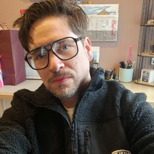 A person wearing glasses and a black fleece taking a selfie.