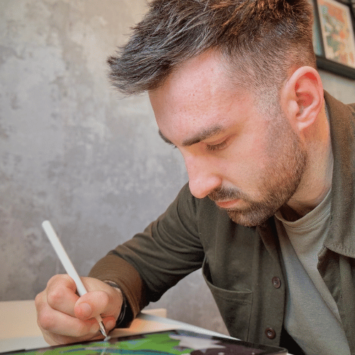 A person with short brown hair works at a desk. It's a close-up shot and they are drawing.