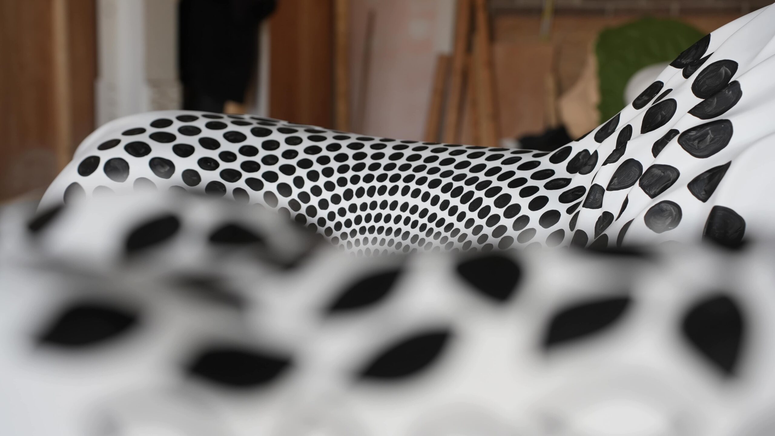 An image of a pair of sculptures - they are white and covered in black dot spiral patterns. One sculpture is close to the camera and out of focus, the other is further away but in focus.