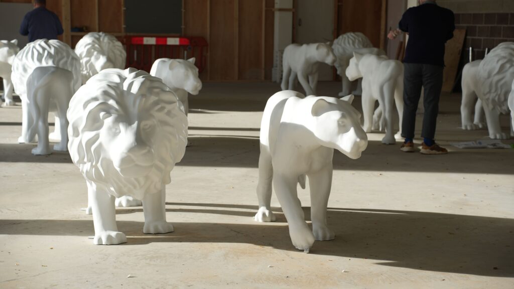 A photograph of lion sculptures in an empty warehouse. Sunlight streams into the room and illuminates the blank, white lion sculptures.