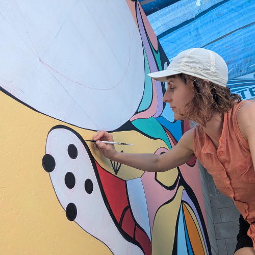 A person wearing a white baseball cap works on a colourful mural.
