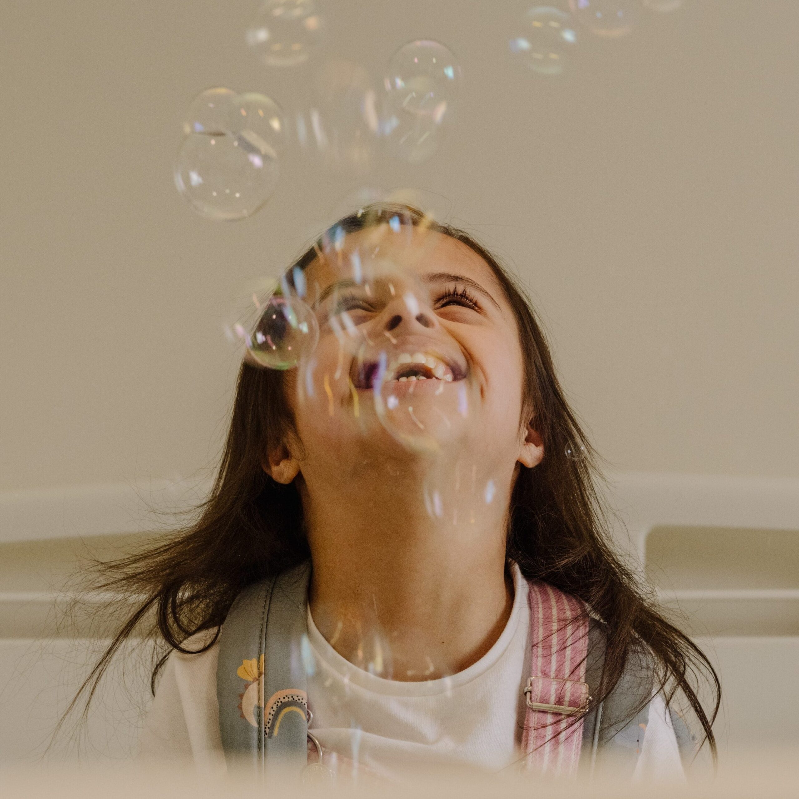 A child looks upwards as bubbles plume out in front of their face. They have a huge smile on their face.