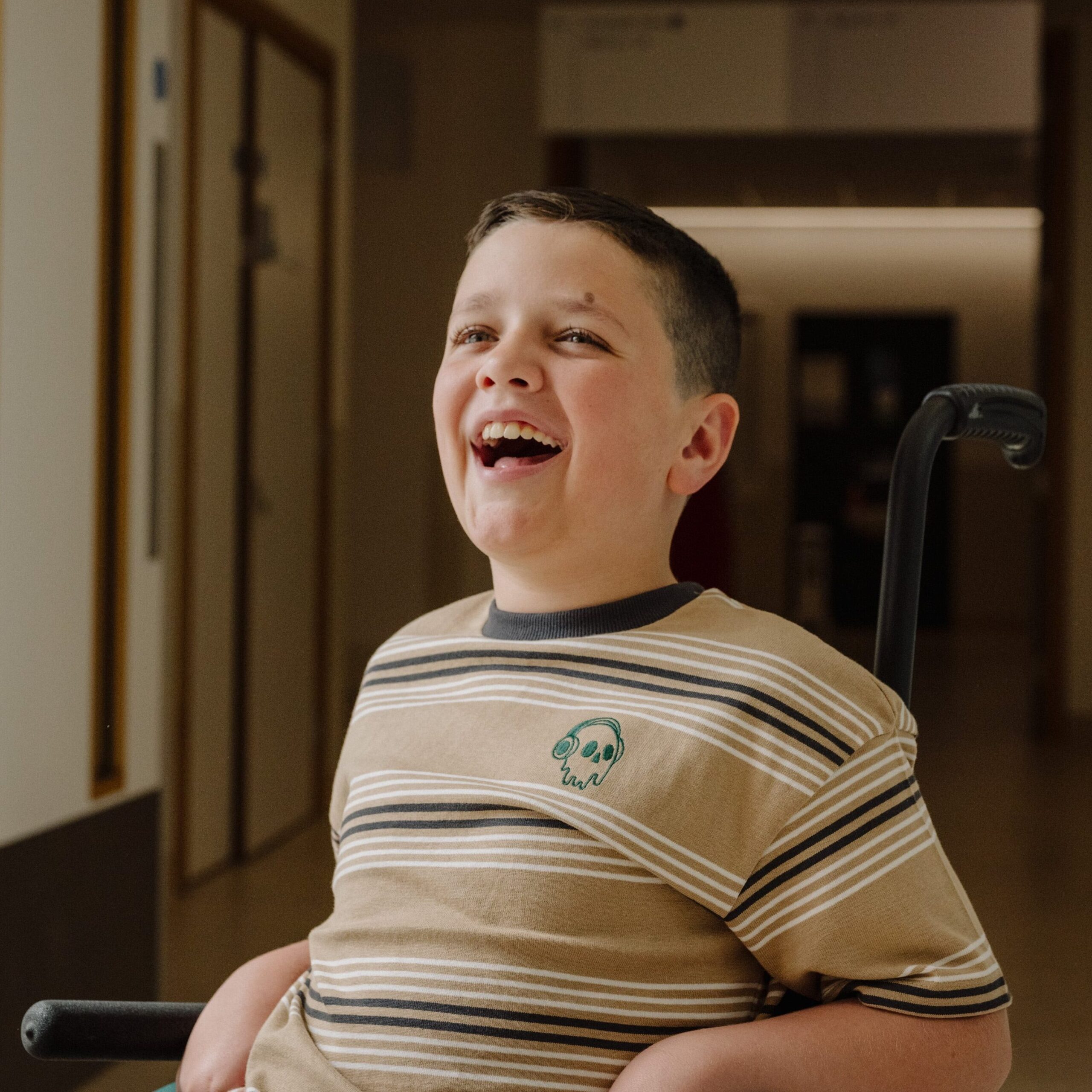 A child in a striped t-shirt smiles to someone just off camera.