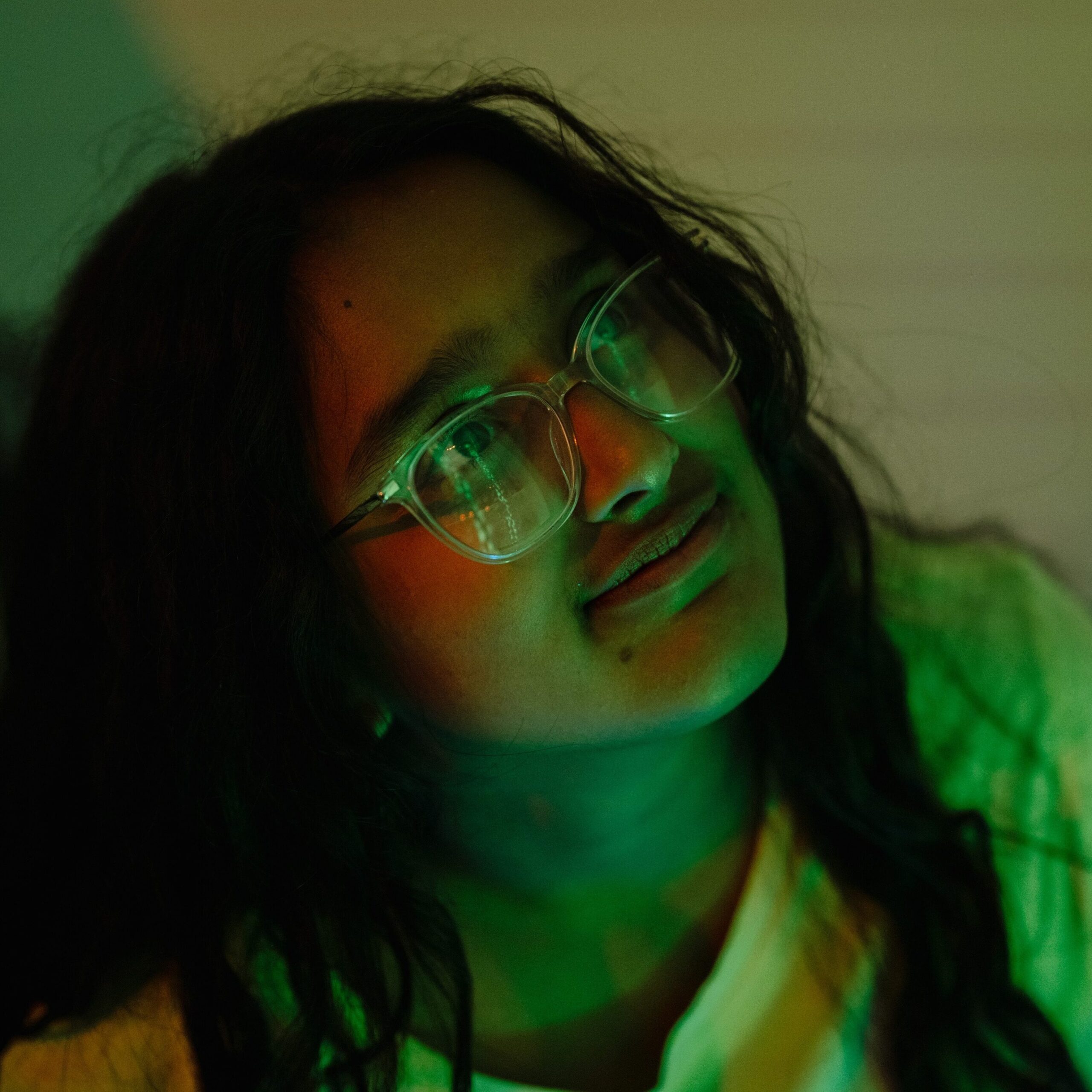 A child with glasses and dark hair is illuminated green by a light in a sensory room. They are looking inquisitively upwards.